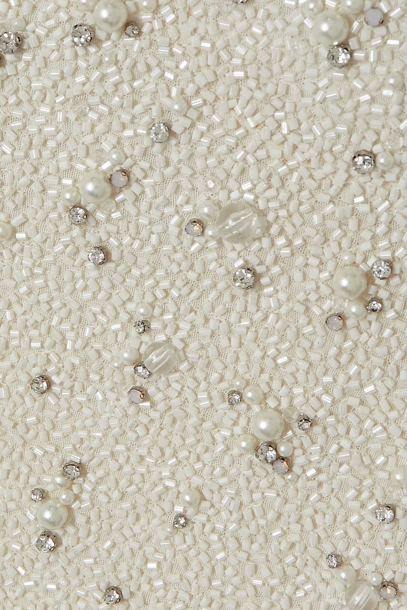 Close-up of a cream-colored beaded fabric with dense sequins, faux pearls, and clear rhinestone accents.