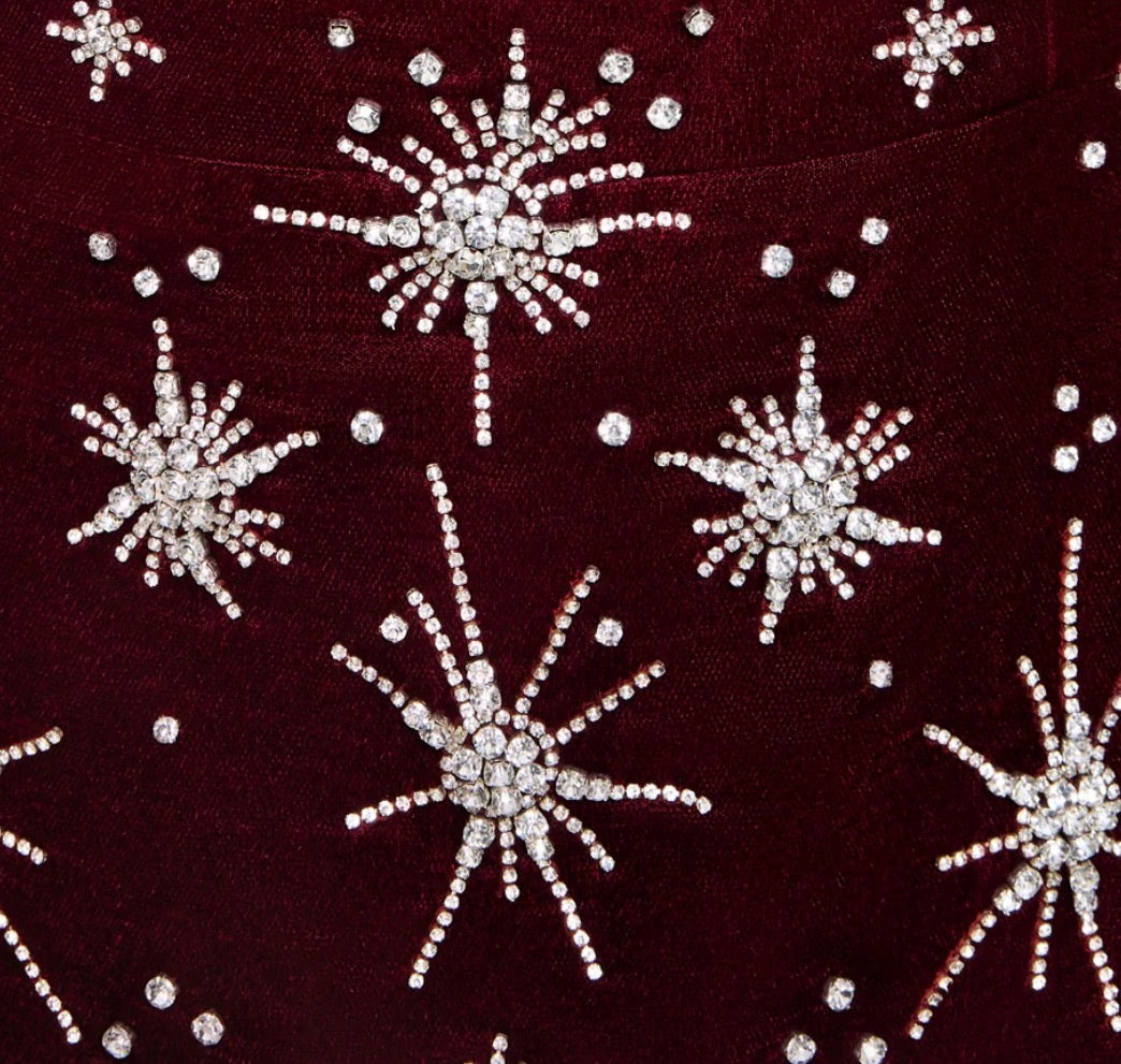 Close-up of a deep burgundy velvet fabric decorated with silver and clear crystal starburst brooches and scattered crystal dots.