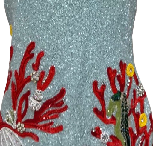 Close-up of a glittery light blue fabric with embroidered red coral, white pearls, and a green seahorse motif.
